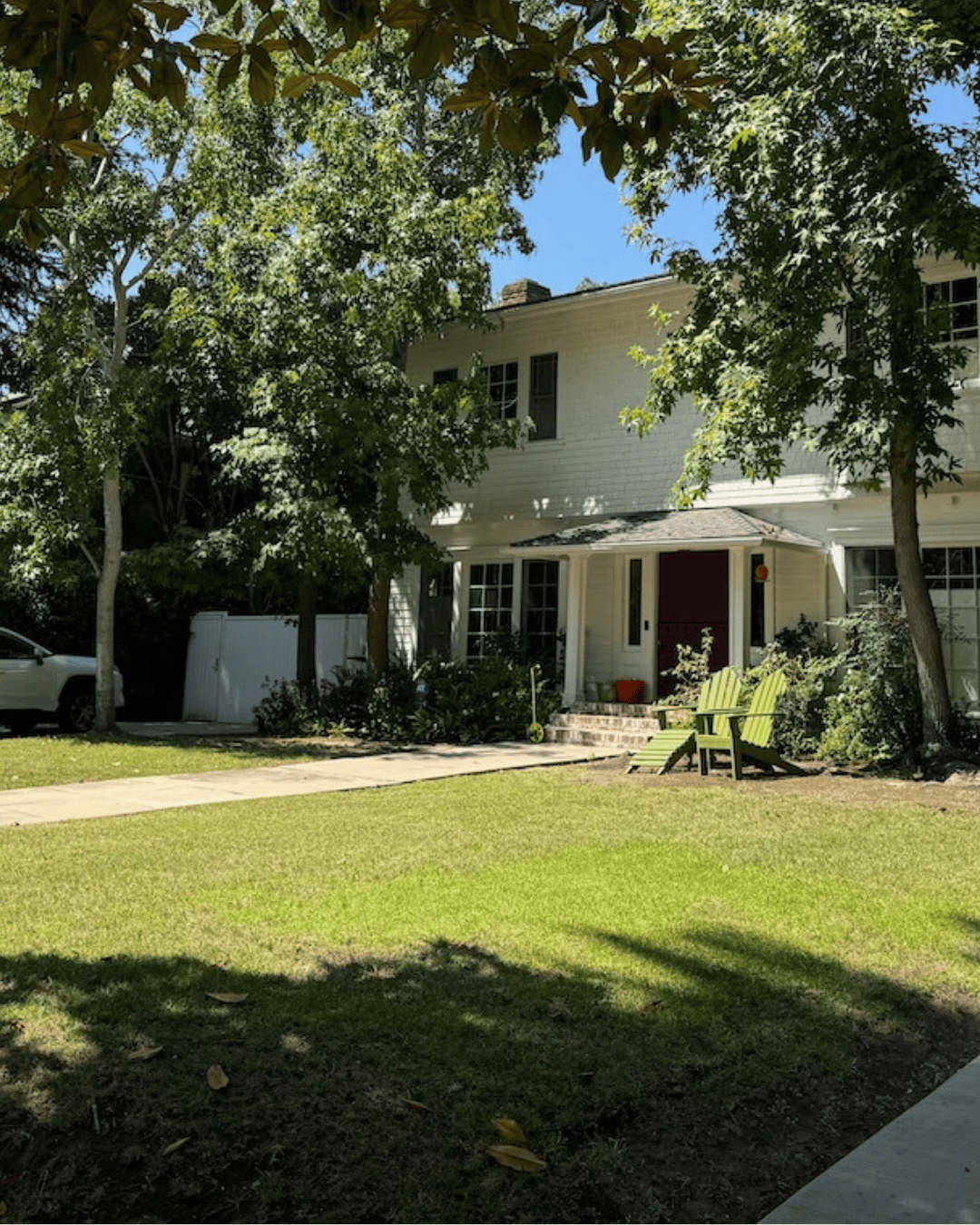 Before photo of the property showing a traditional front lawn with mature trees and two chairs in front of a white two-story home.